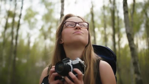 Mujer caucásica feliz con cámara vintage disfrutando de vacaciones en la naturaleza. Mochilero en el bosque — Vídeo de stock