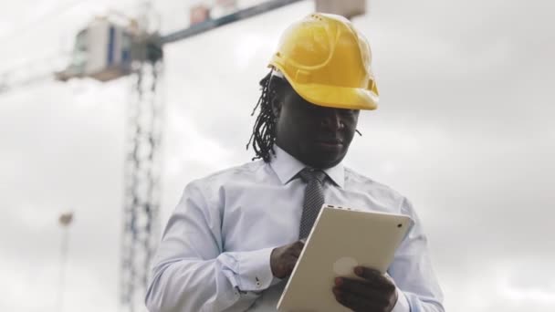 Africký inženýr se žlutým pevným kloboukem pracující na tabletu. Zpomalený pohyb — Stock video