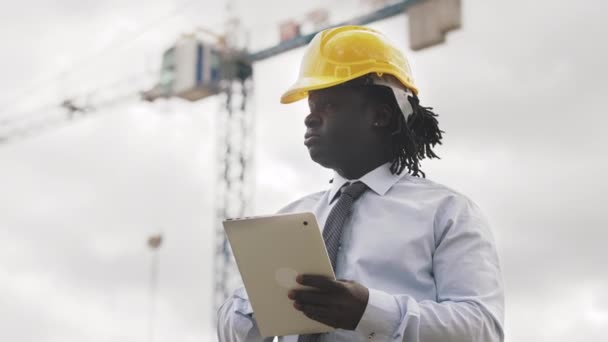 Africký inženýr se žlutým pevným kloboukem pracující na tabletu. Zpomalený pohyb — Stock video