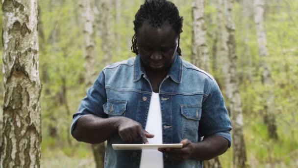 Afrikaanse man die de tablet in de natuur gebruikt. Ik raak het scherm aan. Langzame beweging — Stockvideo