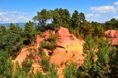 Ocher tepeleri, yeşil ağaçlar ve mavi gökyüzü. Fransa 'nın Roussillon köyü yakınlarındaki Le Sentier des Ocres