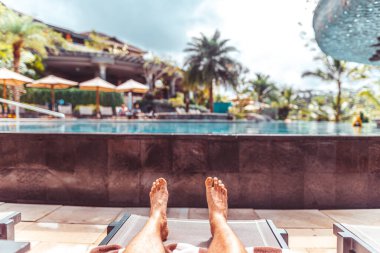 Lüks bir tatil köyünde, tropik bir havuz kenarında yatan bir adam.