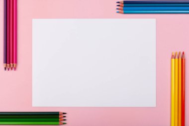 Pembe arka planda beyaz bir sayfa. Her iki tarafında renkli kalemler var..