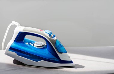 Ütü masasında duran mavi ve beyaz elektrikli ütü.