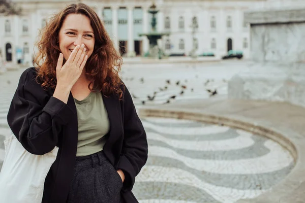 Millennial woman looking at camera laughing. Rossio Square with famous Portuguese pavement in Lisbon, Portugal