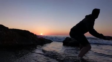 Bacağında küçük dövmesi olan genç bir çocuk gün batımında kayalarda yürüyor.