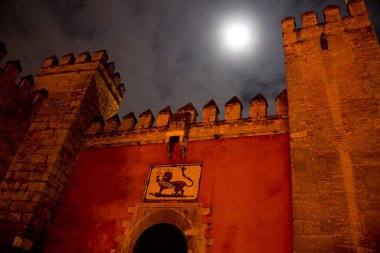 Gece vakti bulutlu gökyüzü ve dolunay ile Sevilla, Endülüs, İspanya 'daki Berberi kalesinin ön kapısı.