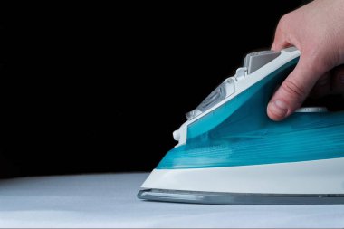 Siyah arka planda beyaz bir bezin üzerinde duran turkuaz demiri tutan bir adamın eline yakın plan. Metin eklemek için boş boşluk.