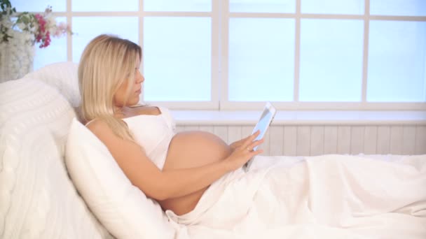 Gravid kvinna avkopplande på säng med surfplatta — Stockvideo