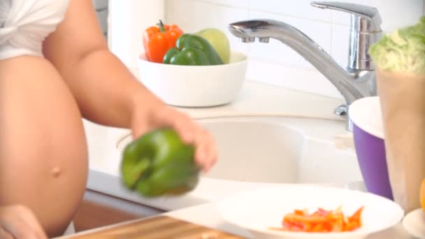 Zwangere vrouw wast en snijdt peper in de keuken. — Stockvideo