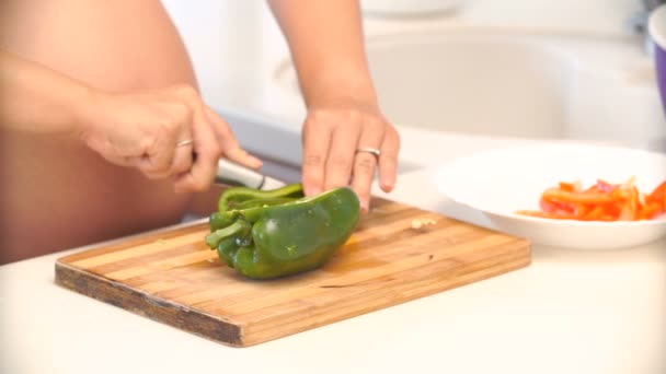 Mujer embarazada corta pimienta en la cocina. verduras para ensalada — Vídeo de stock