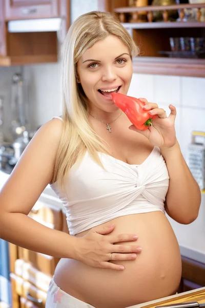 Mujer comiendo pimienta en la cocina y sonríe , — Foto de Stock