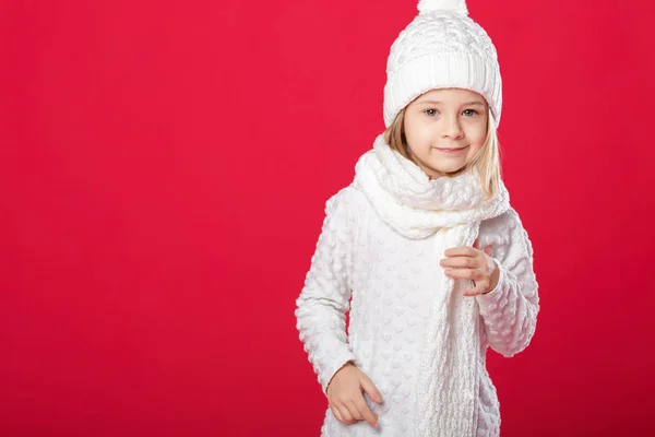 Bir beyaz şapka ve atkı kırmızı backg üzerinde gülümseyen küçük sarışın kız — Stok fotoğraf