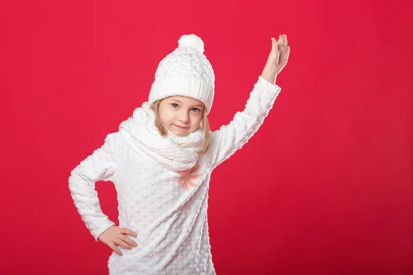 Pequeña chica rubia sonriente en un sombrero blanco y bufanda en el respaldo rojo — Foto de Stock