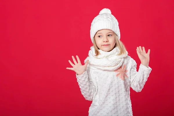 Petite fille blonde souriante dans un chapeau blanc et écharpe sur fond rouge — Photo