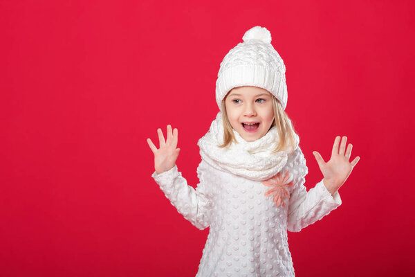 little smiling blonde girl in a white hat and scarf on red backg