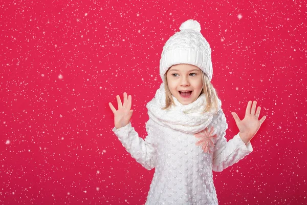 Lilla leende blond flicka i en vit mössa och halsduk på röda backg — Stockfoto