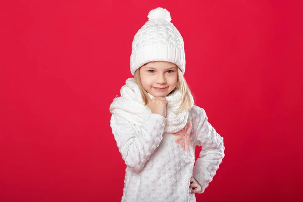 Malá usměvavá blondýnka v bílé čepici a šálu na červené pozadí — Stock fotografie