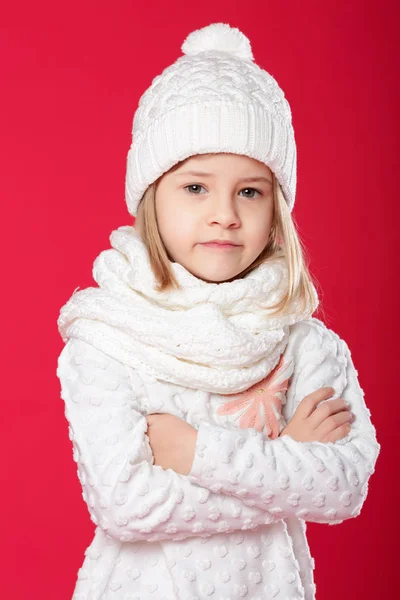 Malá usměvavá blondýnka v bílé čepici a šálu na červené pozadí — Stock fotografie