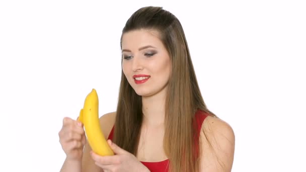 Красивая девушка ест банан на белом фоне — стоковое видео