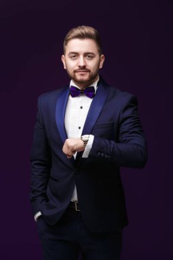 Smokin ve papyon yakışıklı adam saatine bakar. Moda, Festival giyim. koyu arka plan üzerinde emcee