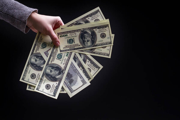 female hand holding a hundred dollar bill on black background. c