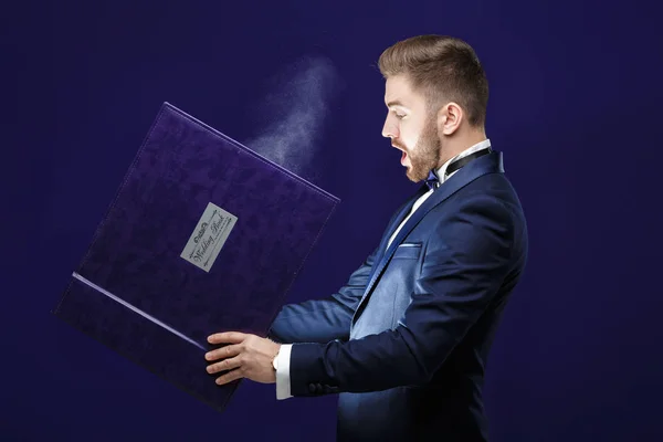 Молодой человек с бородой держит книгу и волшебный свет на темном фоне — стоковое фото