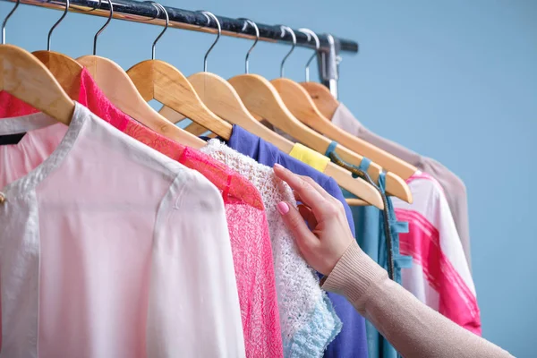 Vrouwelijke hand selecteert kleurrijke kleding op houten hangers op rek in — Stockfoto