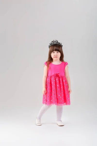 Красива дівчинка в рожевій сукні принцеси з короною на сірому — стокове фото
