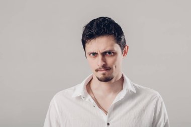 hayal kırıklığına uğramış ve kırgın yakışıklı genç gri arka plan üzerinde Beyaz gömlekli. yumuşak, ışık