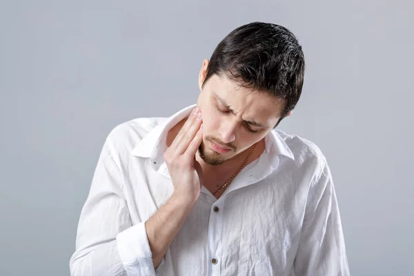 Frustrato giovane bruna uomo in camicia con mal di denti su ba grigio — Foto Stock
