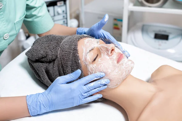 Косметолог наносит маску на лицо молодой женщины и делает массу для лица — стоковое фото