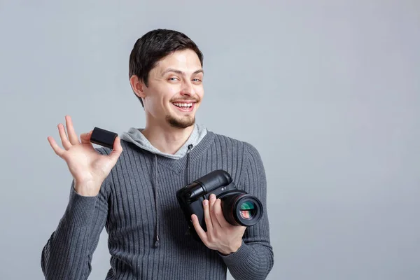 Young smilling photographer in shirt  holds the battery for DSLR — Stock Photo, Image