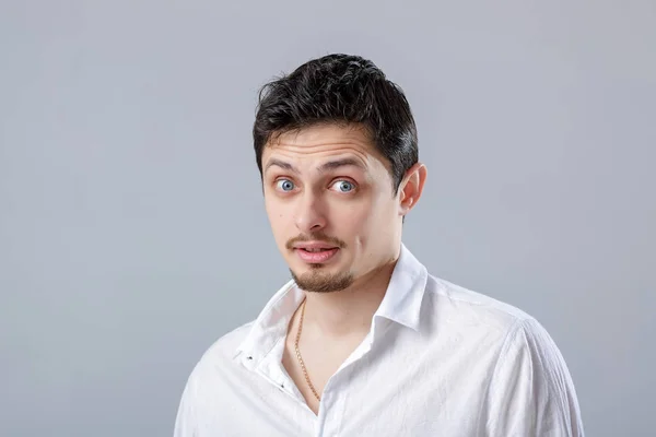 Młody atrakcyjny zaskoczony brunetka człowiek w białej koszuli na szary b — Zdjęcie stockowe