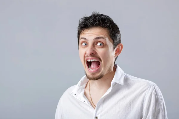 Θυμωμένος νεαρός στο λευκό πουκάμισο ουρλιάζοντας σε ένα γκρι backgroun — Φωτογραφία Αρχείου