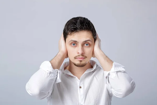 Portrait de jeune homme en chemise blanche couvre ses oreilles avec son ha — Photo