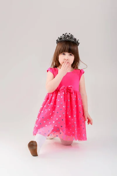 Красивая маленькая девочка в розовом платье принцессы с короной на сером — стоковое фото