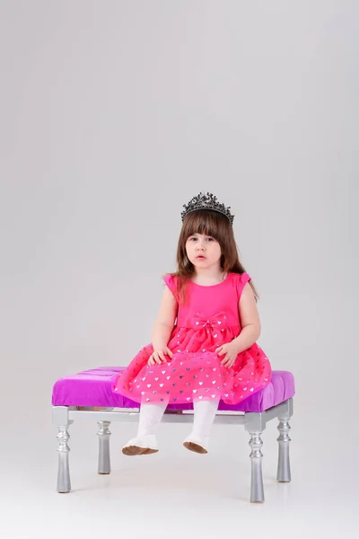 Mooie meisje in roze prinses jurk met kroon zit — Stockfoto