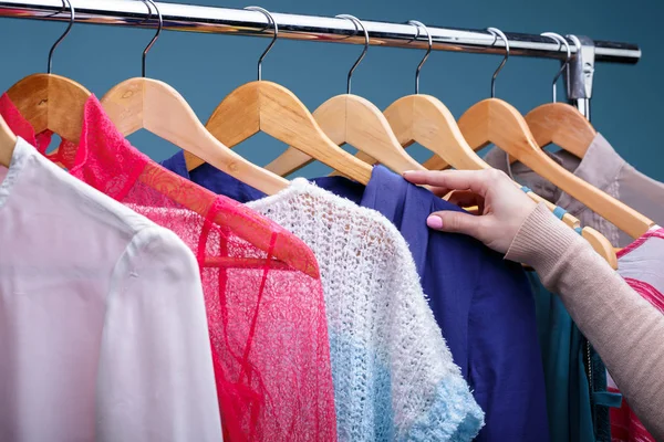 female hand selects colorful clothes on wood hangers on rack in