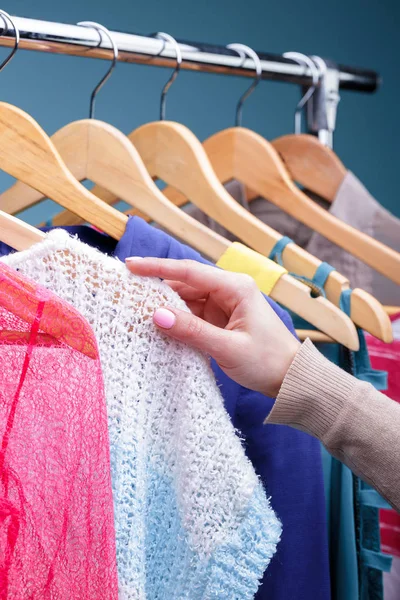 female hand selects colorful clothes on wood hangers on rack in