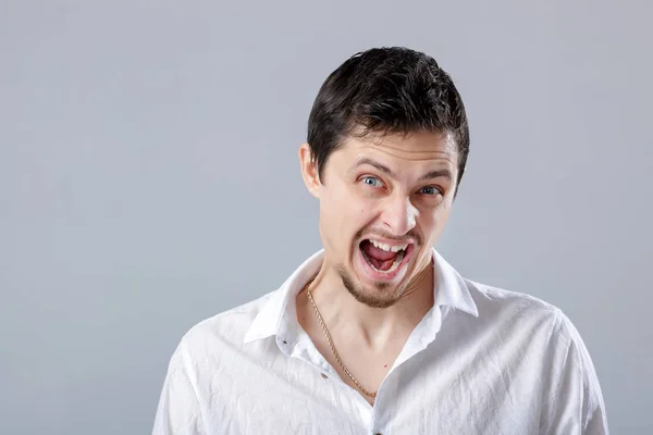 Joven enojado en la camisa blanca gritando en un fondo gris — Foto de Stock