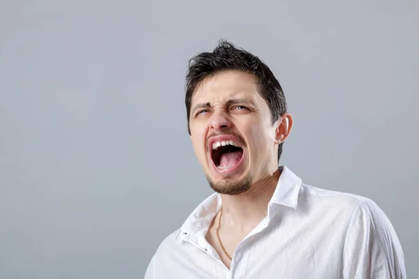 Θυμωμένος νεαρός στο λευκό πουκάμισο ουρλιάζοντας σε ένα γκρι backgroun — Φωτογραφία Αρχείου