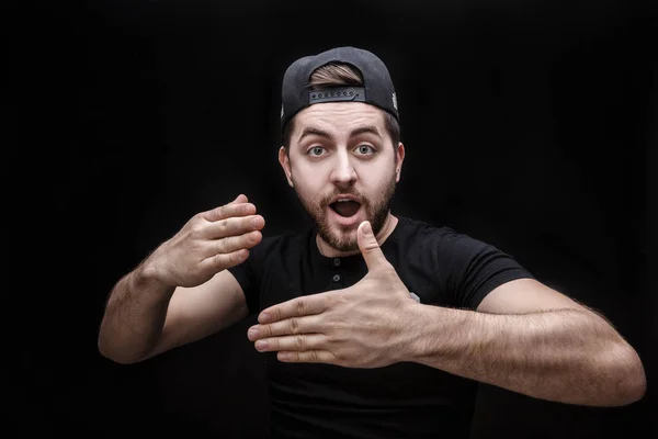 Retrato de hombre joven en camisa y gorra sobre fondo negro hace el truco de la mano —  Fotos de Stock