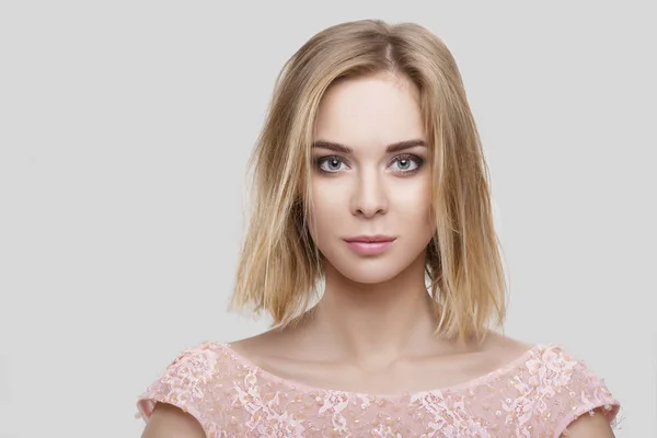 Портрет красивой блондинки с короткими волосами в розовом коктейльном платье на сером фоне — стоковое фото