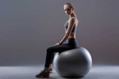 Spor giysileri fitness topu koyu arka plan üzerinde oturan güzel sarışın kızı