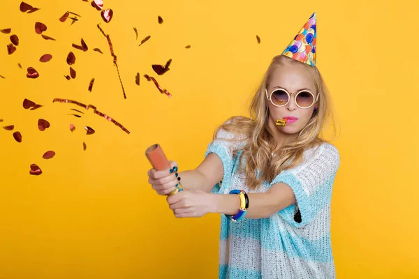 Portret van grappige Blonde vrouw in verjaardag hoed en rode confetti op gele achtergrond. Feest en feest. — Stockfoto