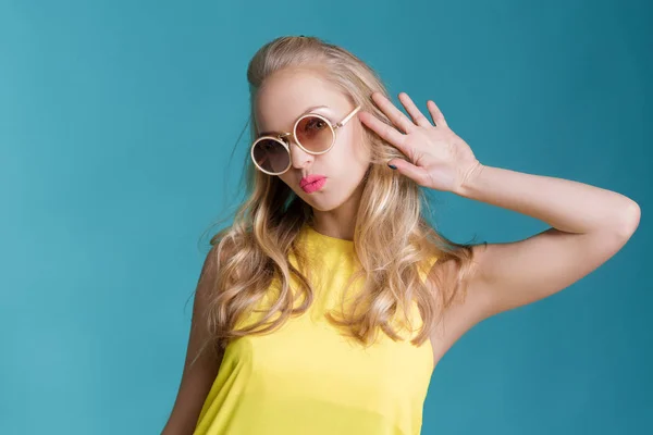 Porträtt av vacker blond kvinna i solglasögon och gula skjorta på blå bakgrund. Sorglösa sommaren. — Stockfoto