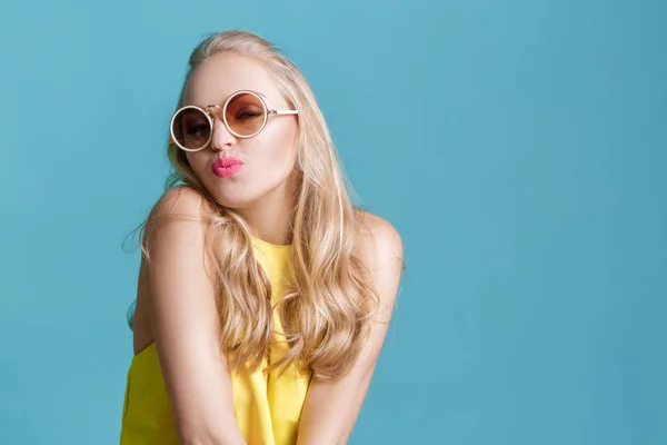 Portrett av en vakker blond kvinne i solbriller og en gul skjorte på blå bakgrunn. Carefree summer . – stockfoto