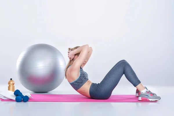 Bela menina loira no sportswear faz exercícios sobre fitness Mat no fundo cinza — Fotografia de Stock