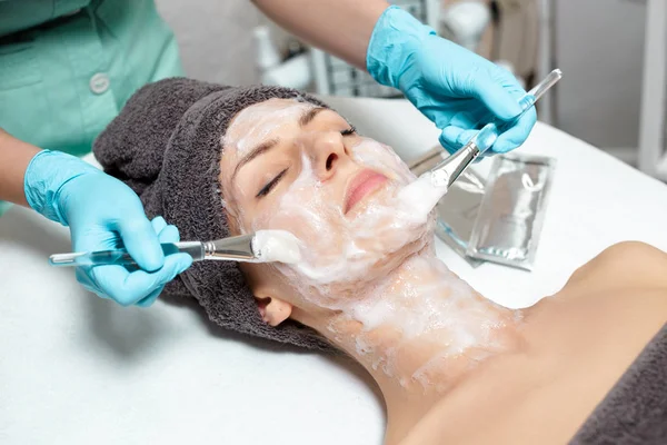 Esteticista aplica mascarilla en hermosa mujer joven en el salón de Spa. procedimiento cosmético cuidado de la piel. Microdermoabrasión — Foto de Stock